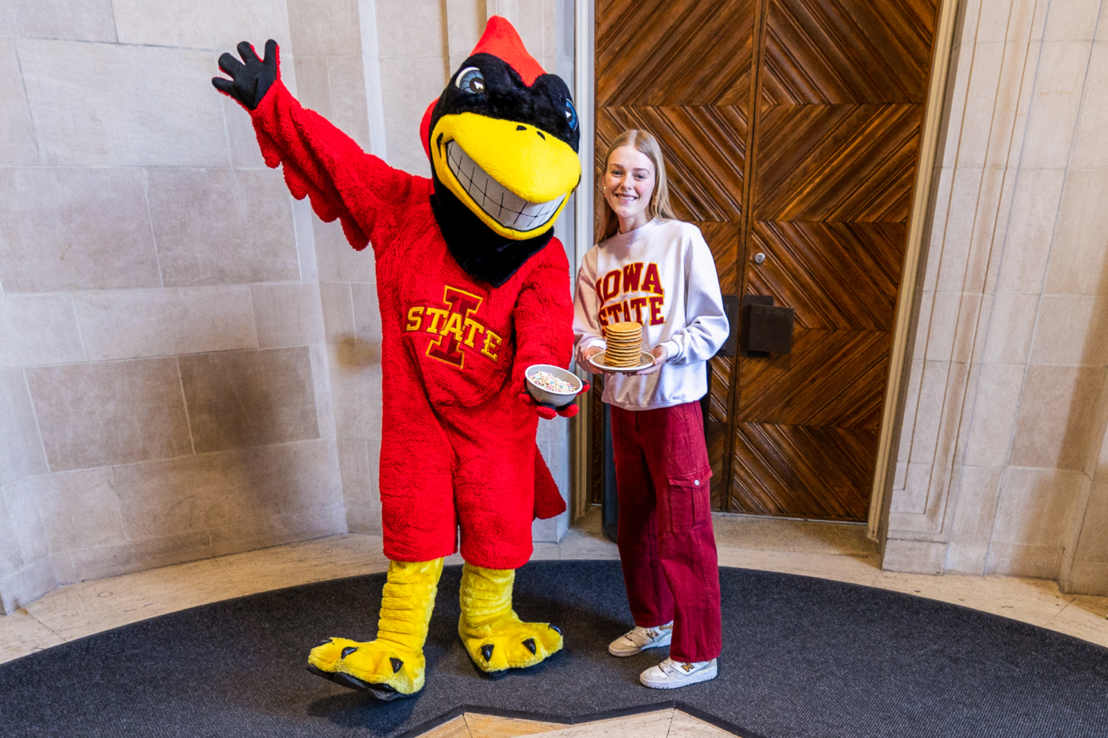Cy holding cereal and standing next to a student holding a stack of pancakes next to the Zodiac in the Memorial Union